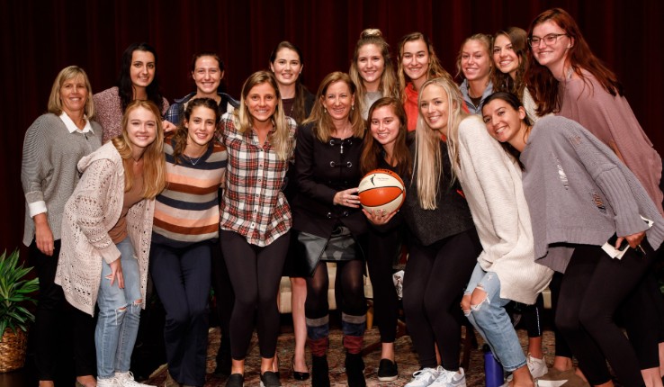 Cathy Engelbert poses with basketball and Lehigh University Women's Basketball team on stage at Gruhn Lecture. 