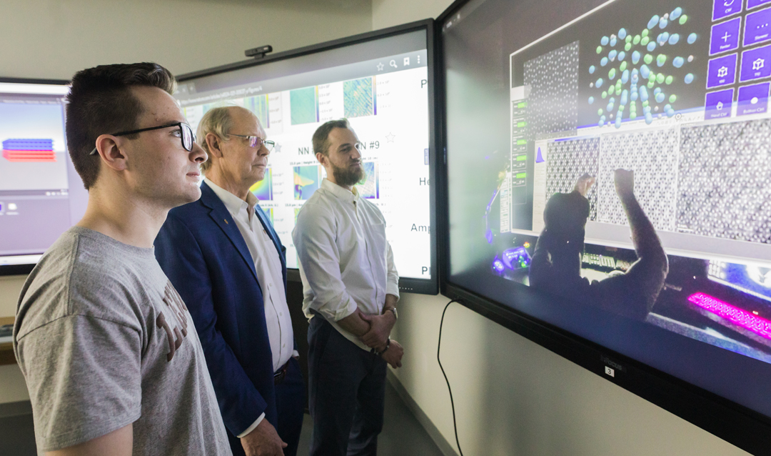 Jack Kellerk, Martin Harmer and David Braun stand in front of large touchscreens in Lehigh University's visualization lab.