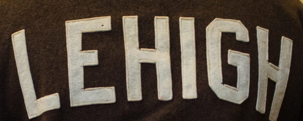 A close up of white "Lehigh" letters sewn on a brown background