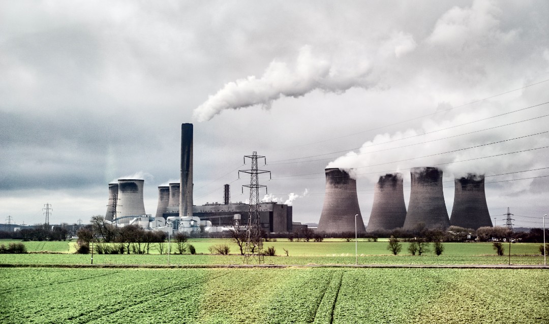 Image of a power plant with clouds of smoke next to grassy field