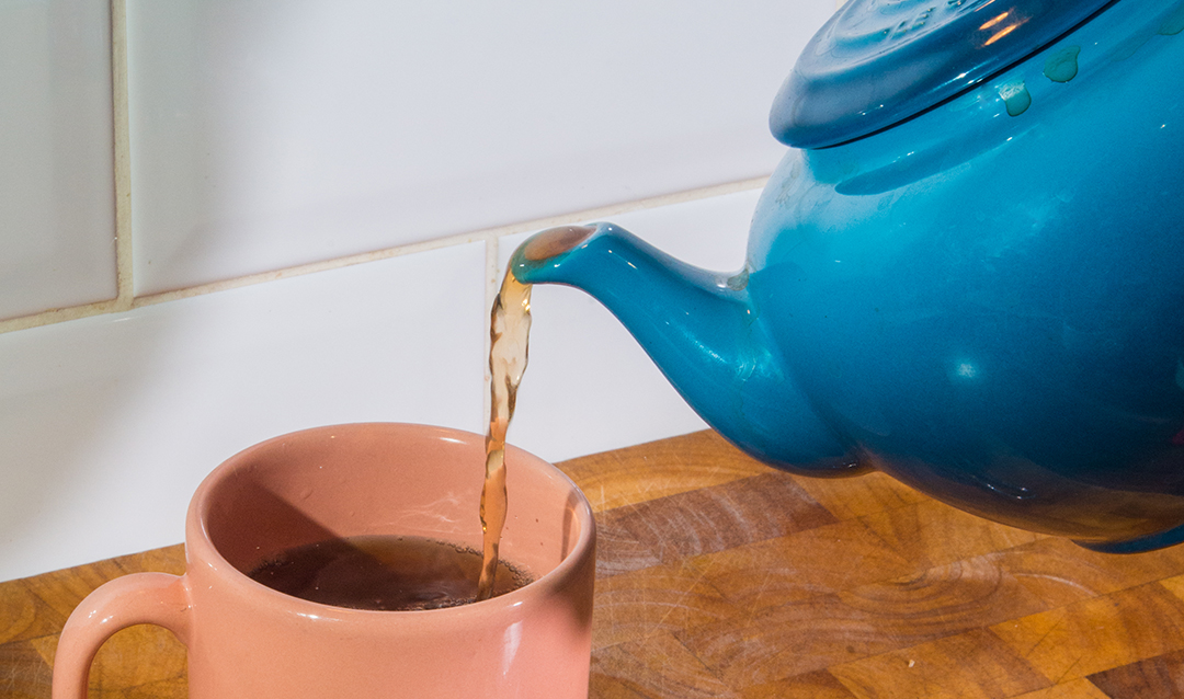 Photo of a blue teapot pouring tea into a pink mug