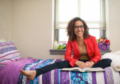 Student sitting on bed in dorm room