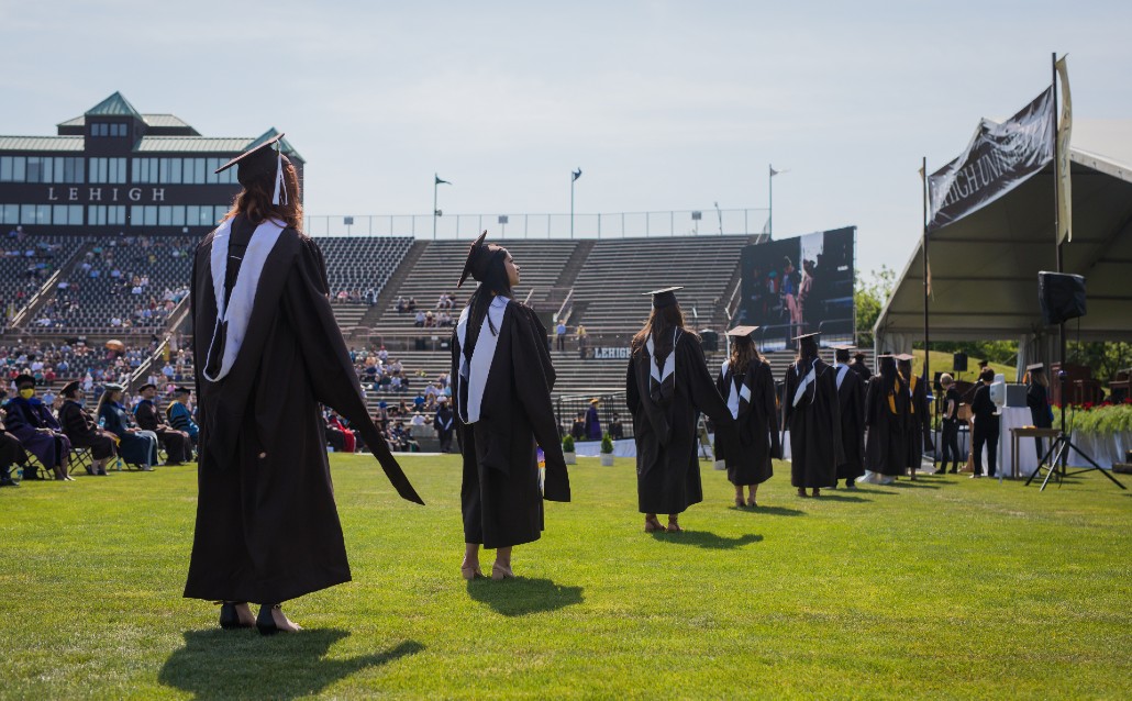 Graduates walk across the grass Goodman Stadium.