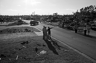 Three people survey the extreme damage caused by a tornado