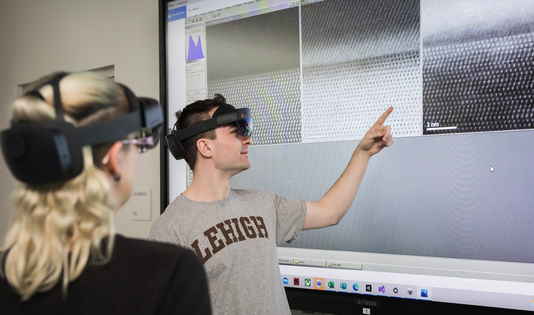 Two Lehigh students wear VR headsets in front of a large touchscreen