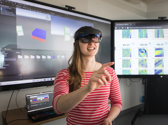 Woman wearing a VR headset in front of two large touchscreens