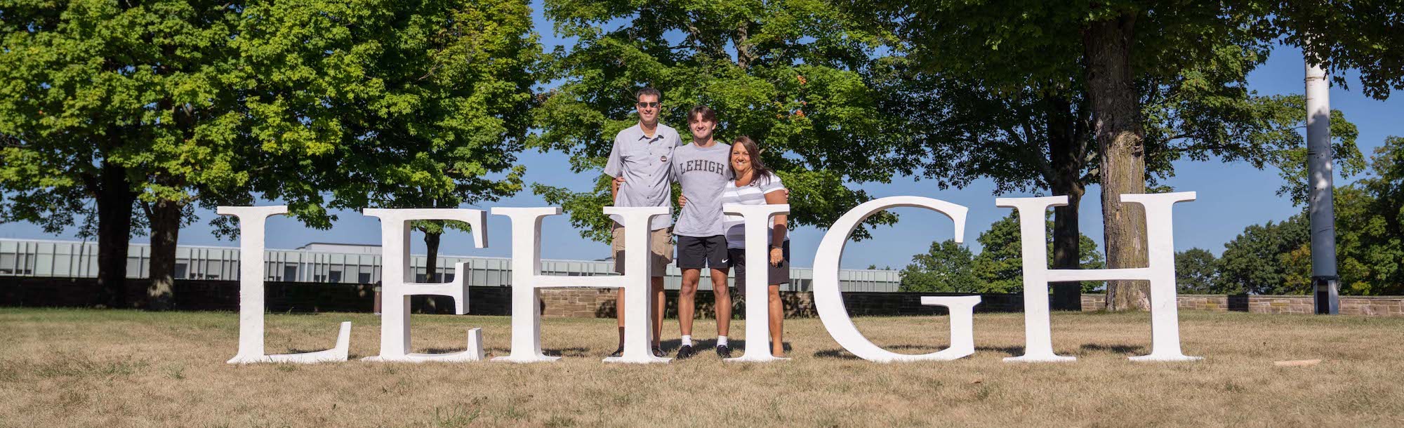 Two parents with a male student standing behind large white letters that spell LEHIGH