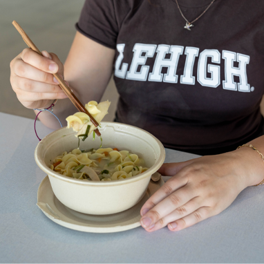 Close up of a person wearing a Lehigh tshirt and eating noodles