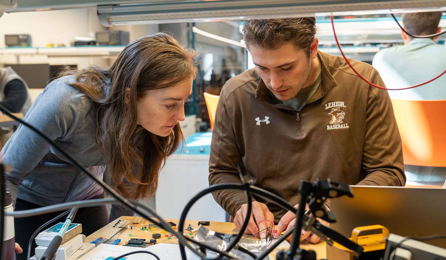 A female professor and male student working on electronics