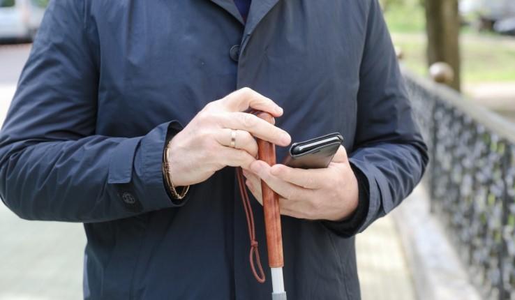 A visually impaired man holding a cane and smartphone.