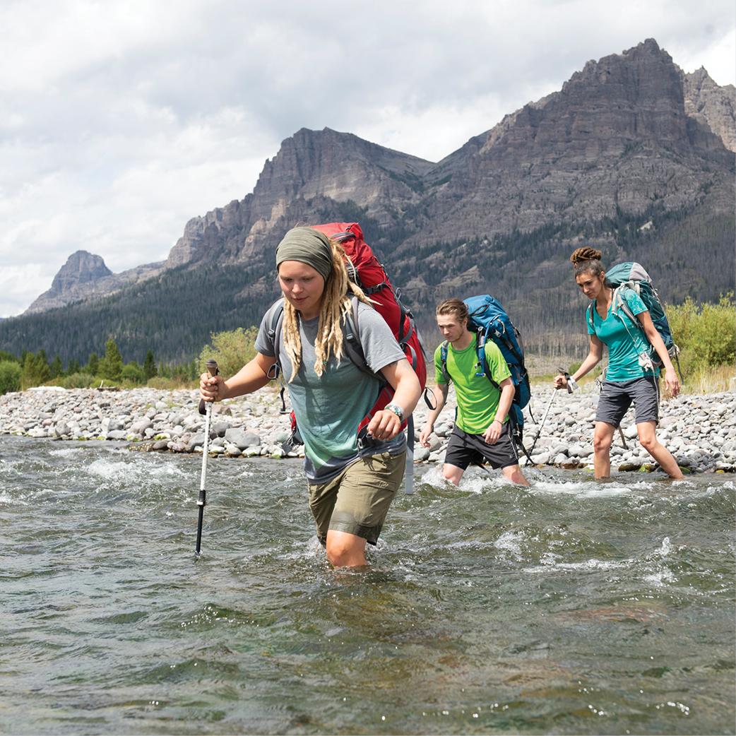 Three students hiking through a river