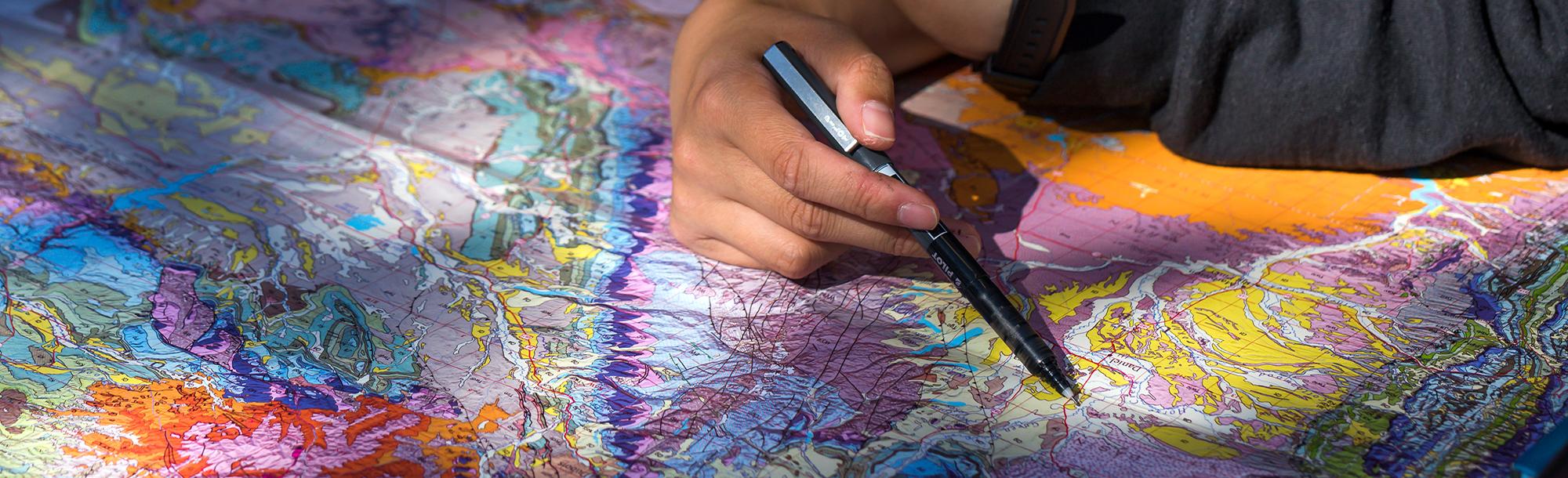 Close up of a hand holding a pen on top of a map