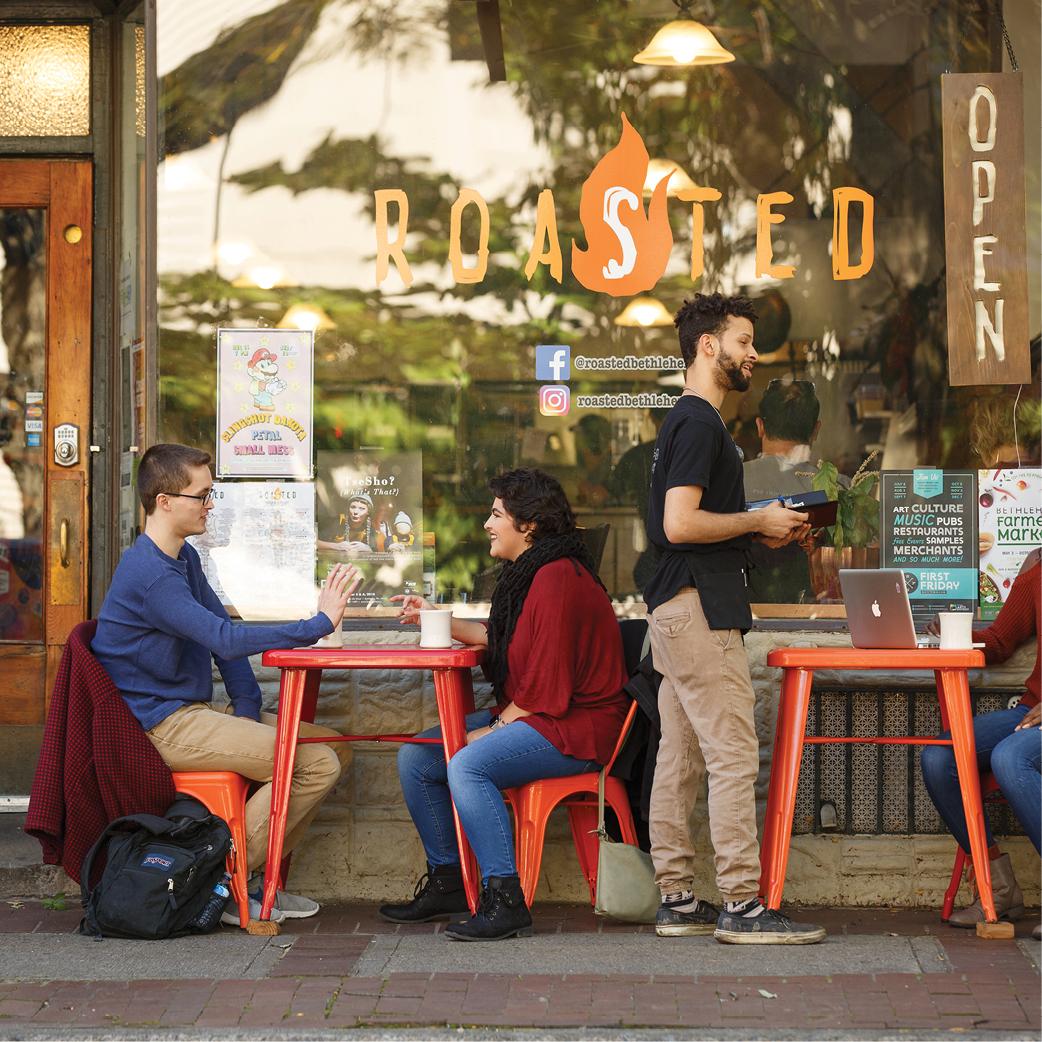 People dining at outdoor tables of a café with glass windows