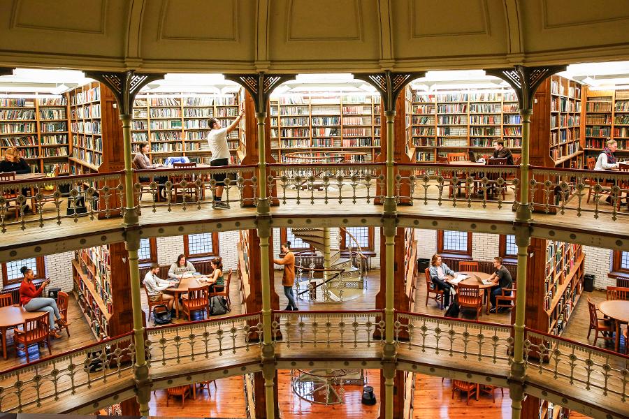 Interior of Linderman Library. A multi-story library with rows of bookshelves filled with books. Each floor has an open balcony with railings and tables where people are reading and studying. The overall structure has a historic and ornate design with warm lighting.