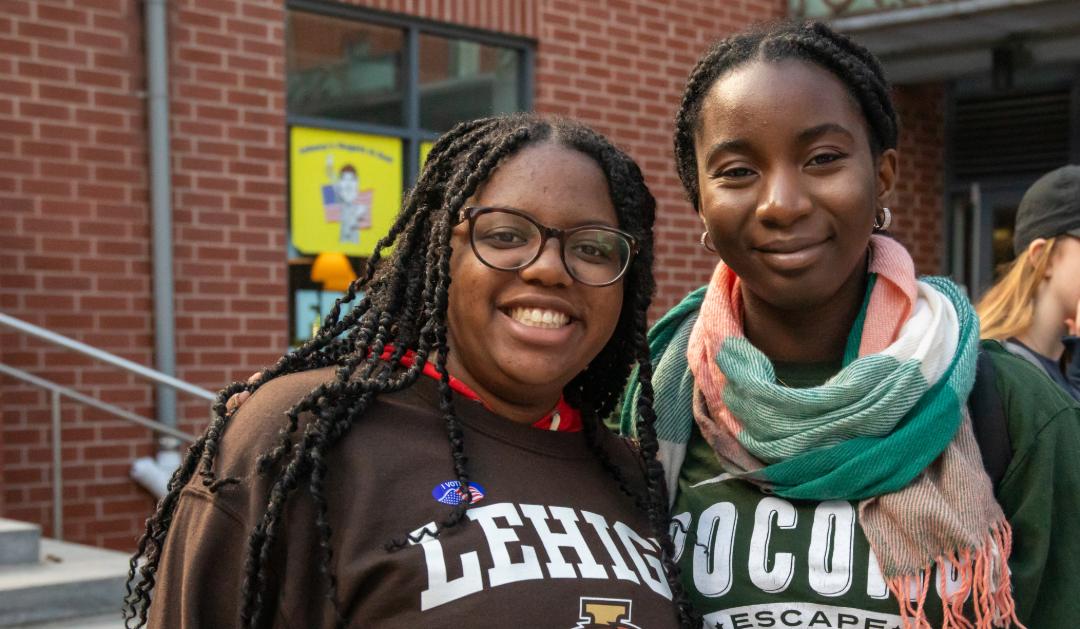 Two Lehigh students smile and pose for a picture together, one wearing an "I voted" sticker.