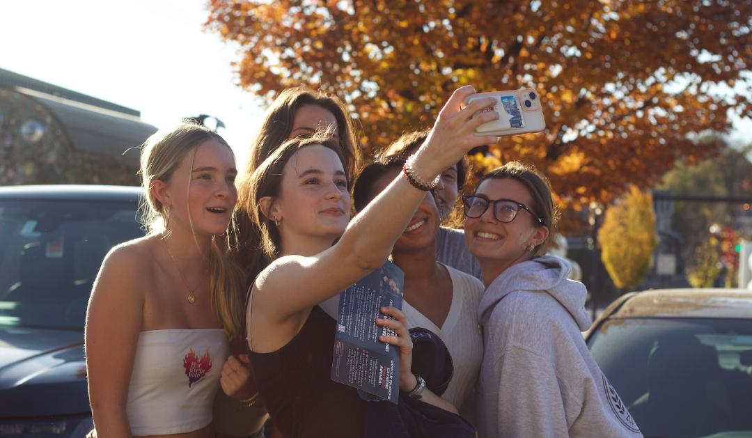 A group of young women take a selfie with voting materials in hand.