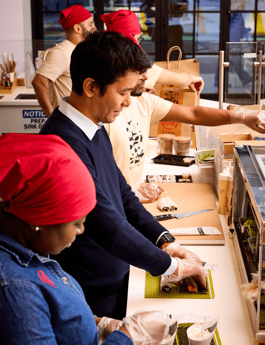 Kevin Takarada ’06G creates a sushi roll alongside employees at a MakiMaki Sushi in New York City.