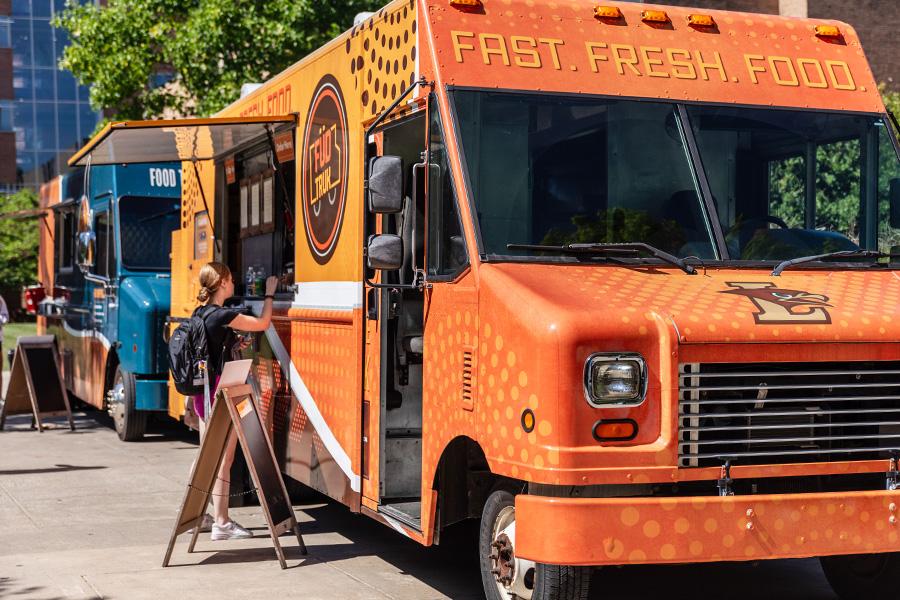 A female student is standing at the window of a bright orange food truck