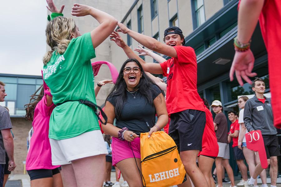 A group of people wearing colorful shirts and sunglasses help students move into their dorms.