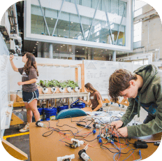 Three students in a modern lab; one writes, one works with electronics.