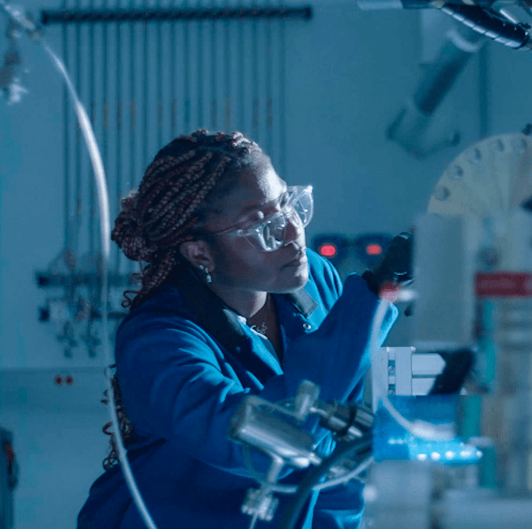 Scientist wearing safety glasses examines equipment in a lab.