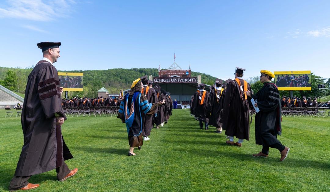 Photograph of graduates walking on a field toward the Lehigh University Commencement stage.