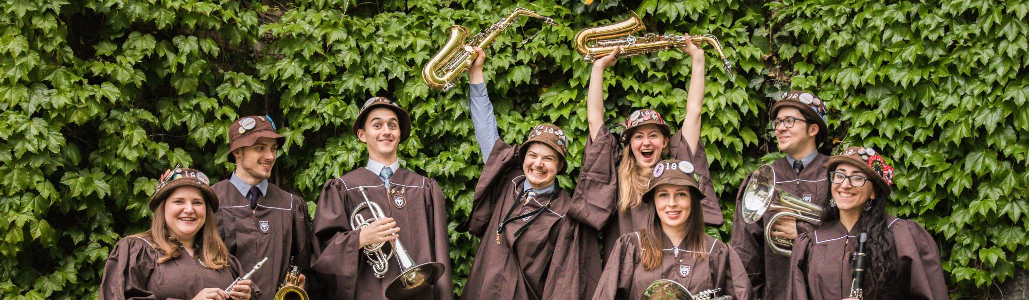 Students lined up in front of an ivy wall with caps and gowns