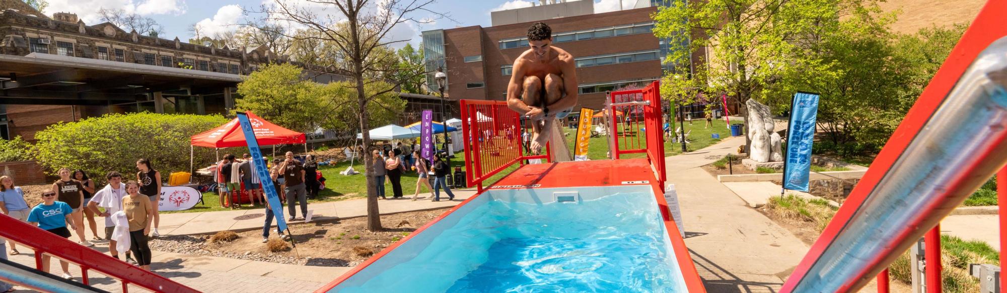 A student jumping into a pool during a campus event
