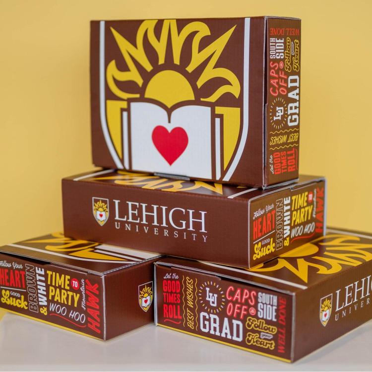 Stacked brown Lehigh University graduation boxes with sun logo, book, and heart.