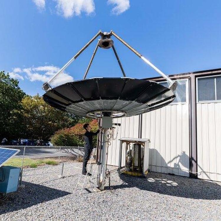 Engineer adjusts a large, dark solar concentrator dish in an outdoor setting.