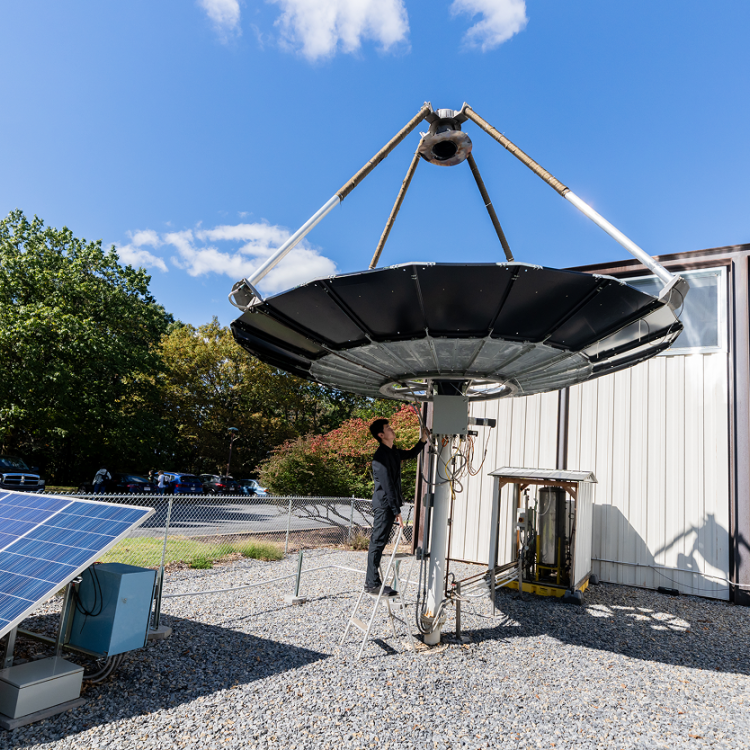 Person working on a large satellite dish next to solar panels.