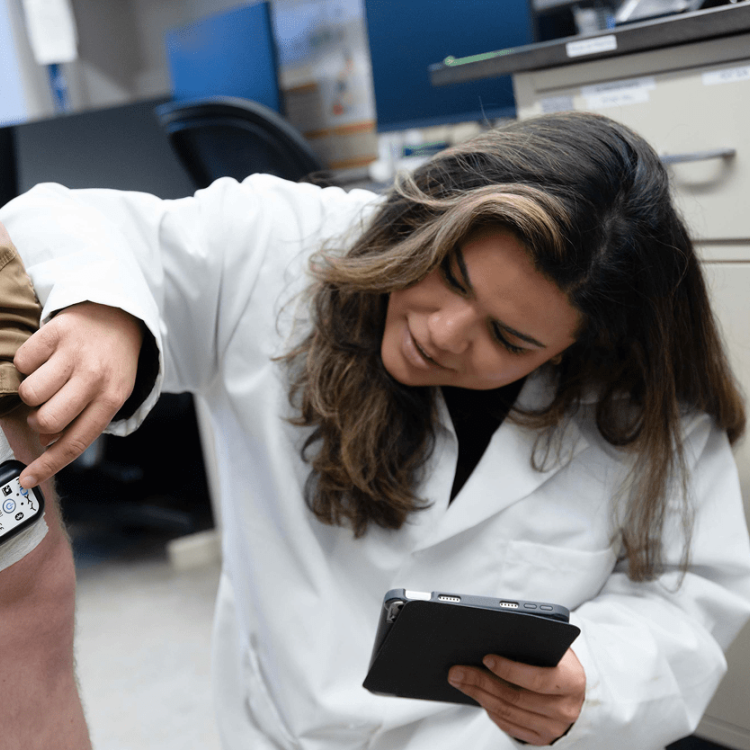 Scientist attaches device to person's leg, holding tablet.