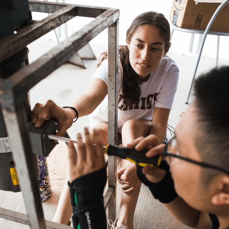 Two people working on a metal frame with tools.