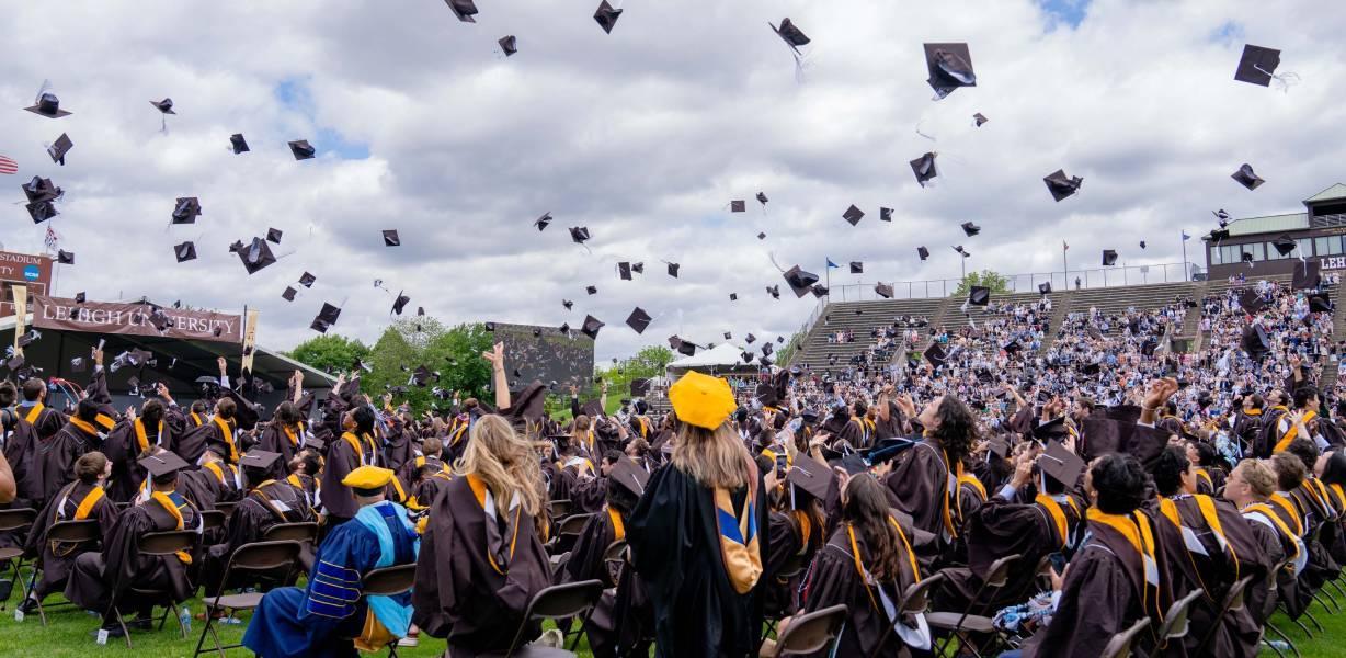 Graduates throwing their caps in the air at an outdoor graduation ceremony