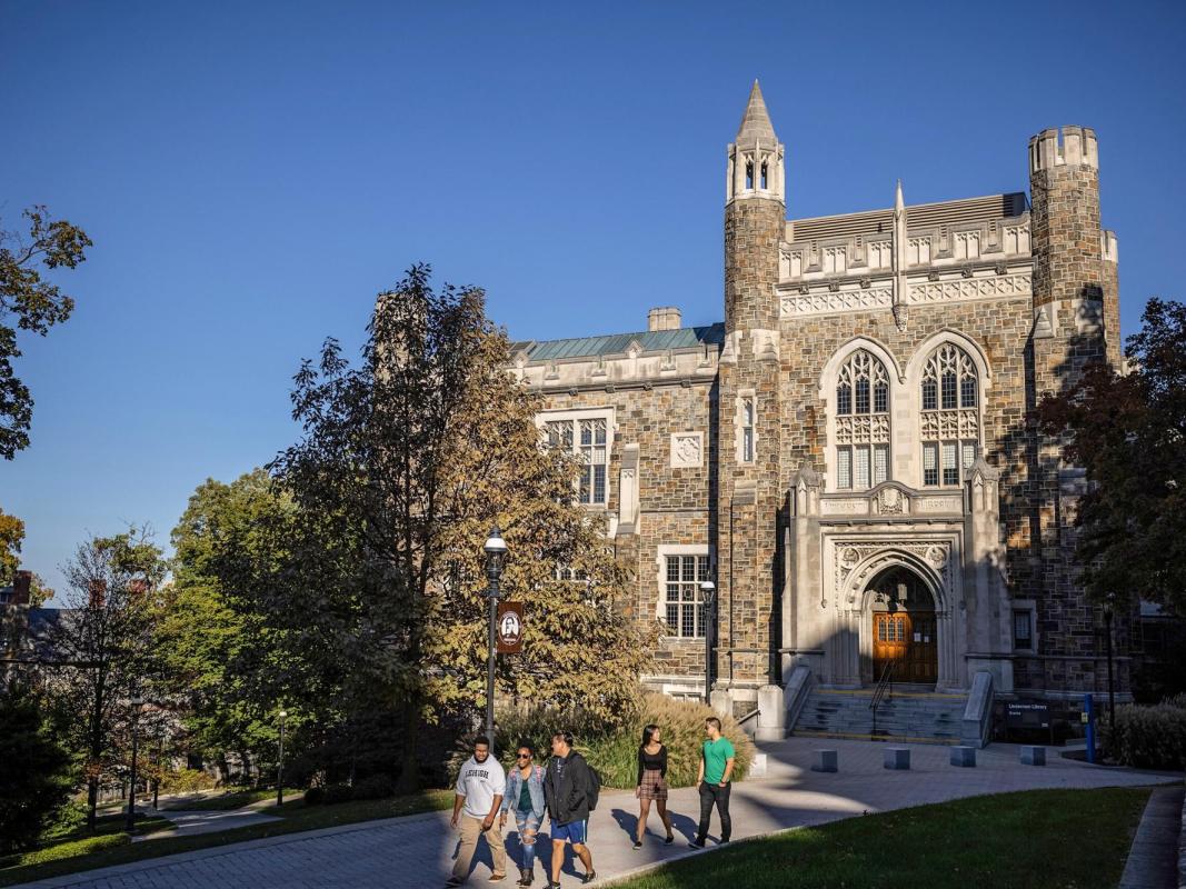 Students walk on a sunny day toward a stone university building.