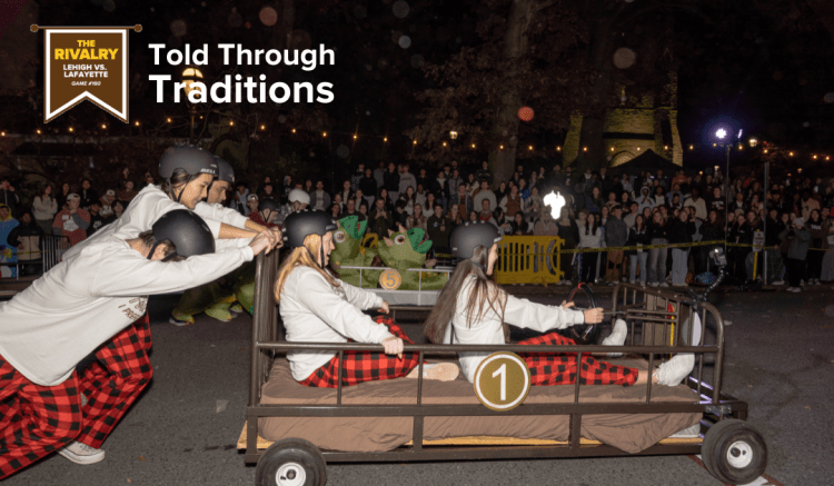 A team of students, all wearing white shirts with red and black plaid pajama pants, race their bed in front of onlookers