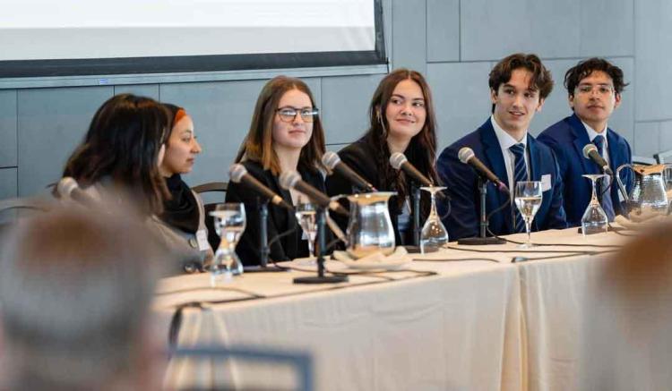 A panel of five young adults seated at a table with microphones, discussing an event.