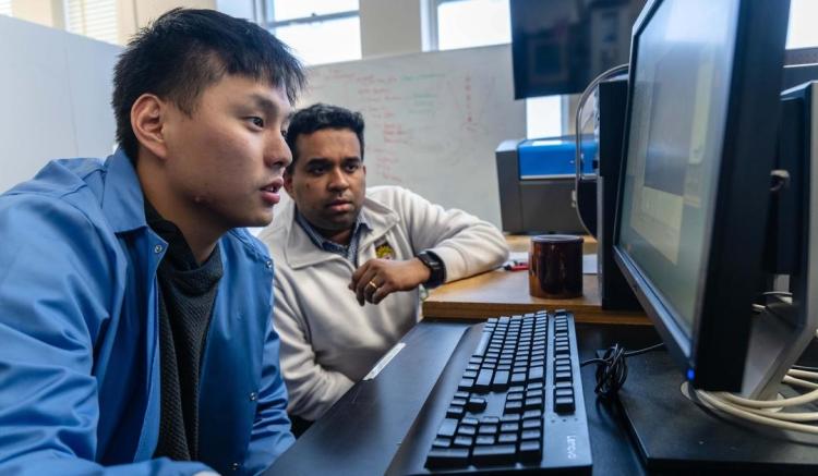 Dr. Dhruv Seshadri, assistant professor in the department of bioengineering collaborating at a computer with student in lab coat.