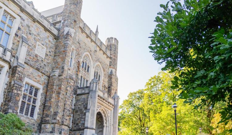 Photograph of a stone gothic university building and green trees on a sunny day.