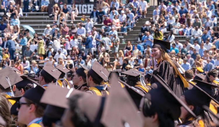Photograph of graduates in brown and gold regalia at a crowded Lehigh University commencement.